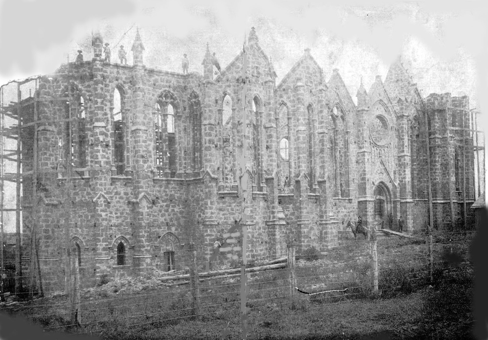 Fotografia de 1907: a Catedral ainda sem cobertura, com trabalhadores sobre as paredes e um homem a cavalo em frente à fachada.
