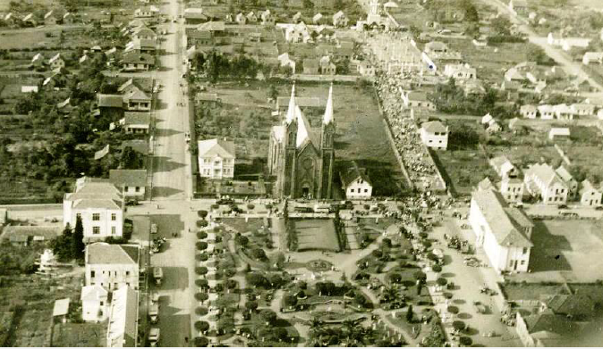 Vista aérea de Vacaria com a Catedral no centro do quarteirão, cercada pela praça arborizada, ruas e casas ao redor.